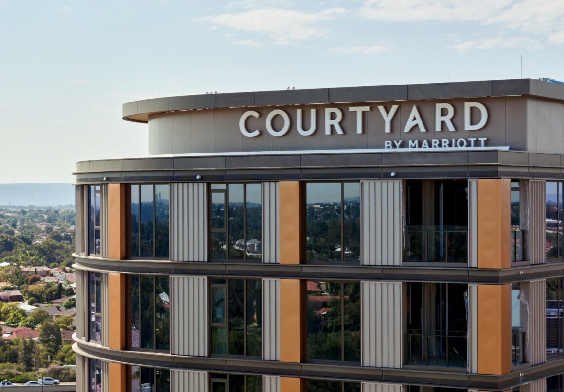 A wide angle view of the outside of The Courtyard By Marriott Hotel with a sky in the background